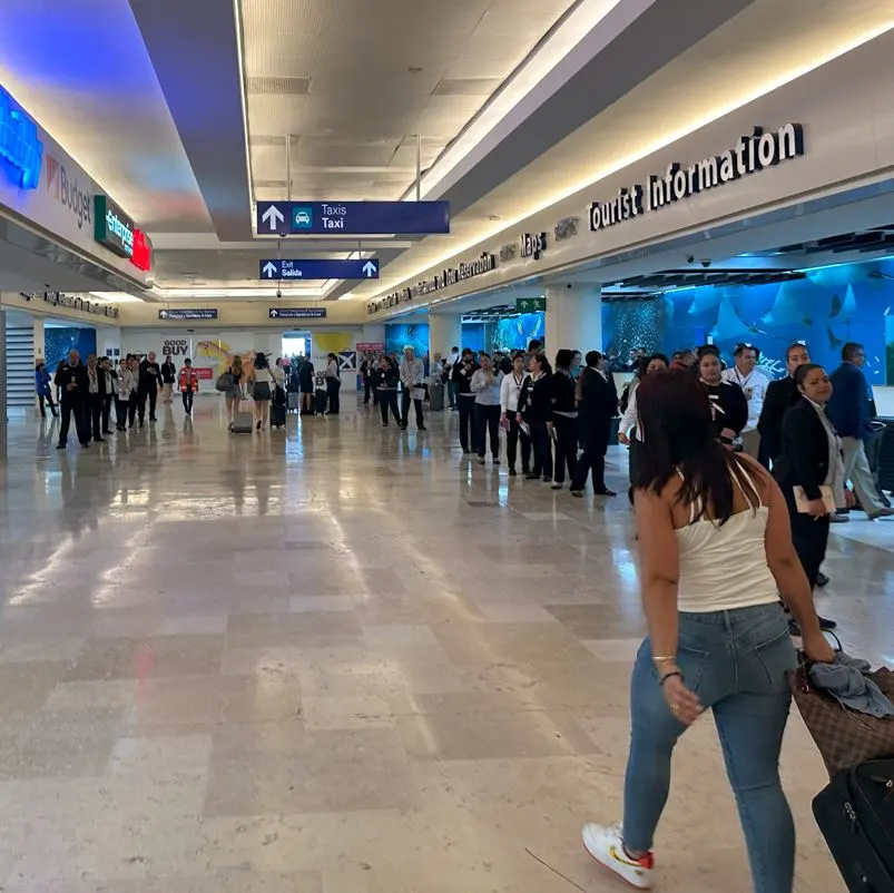 woman walking through airport with suitcase with timeshare idividuals lined up along each side of the wall