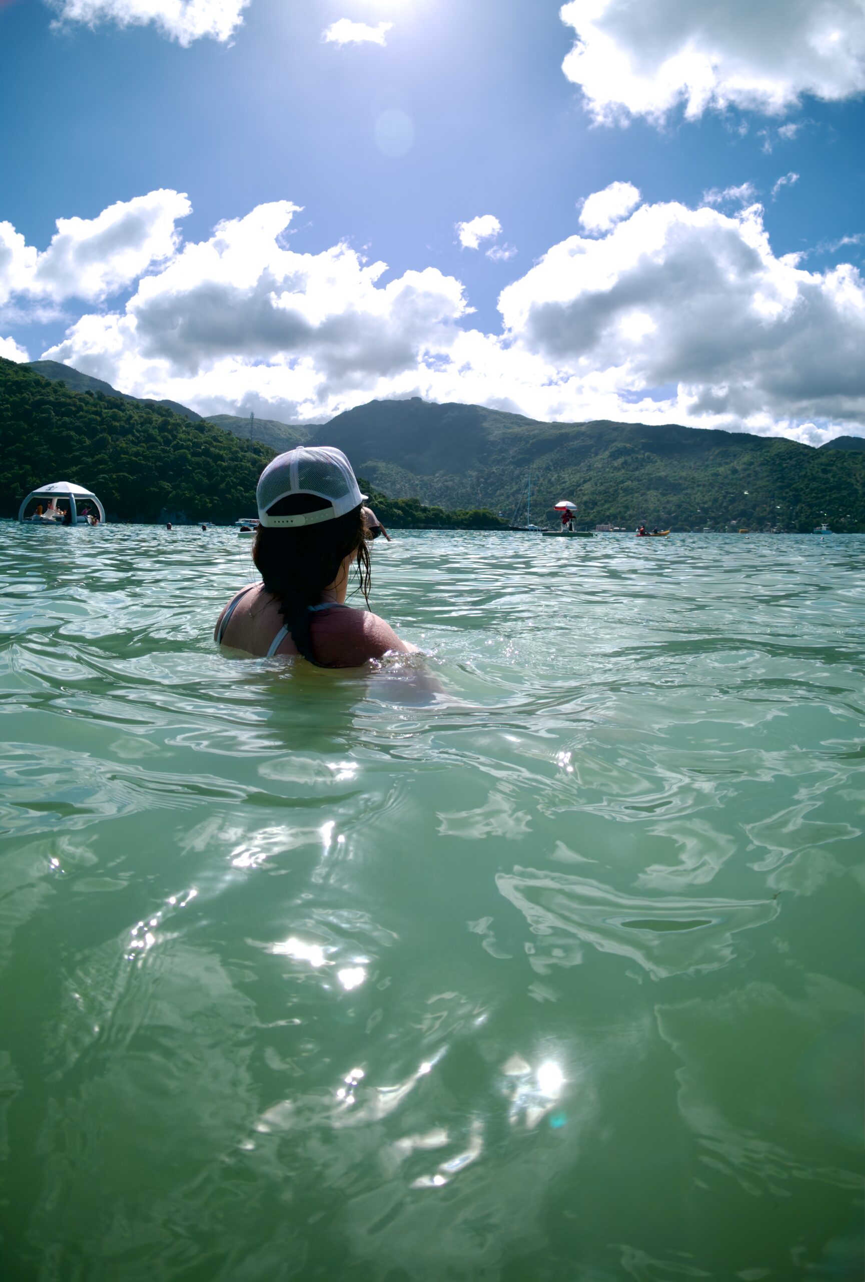 Woman standing in clear turquoise ocean water near green hills